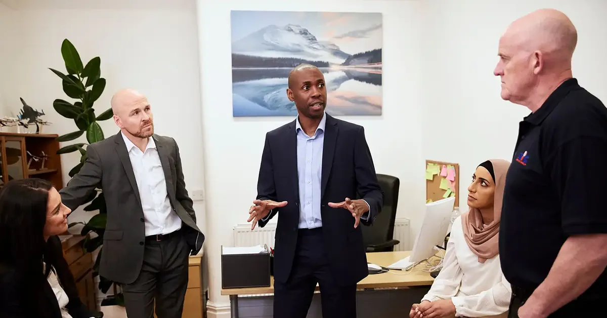 An NIC Local franchisee leads a team meeting in a business office, discussing strategy with staff